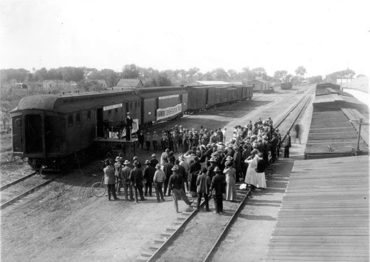 Agriculture Experiment Station Demonstration Train at Mesa, Arizona. Man is standing on a train platform with a cow talking to a group of farmers.